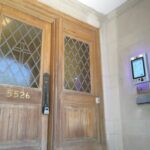 mvi keycom mounted on white stone wall by building entrance with brown wooden doors