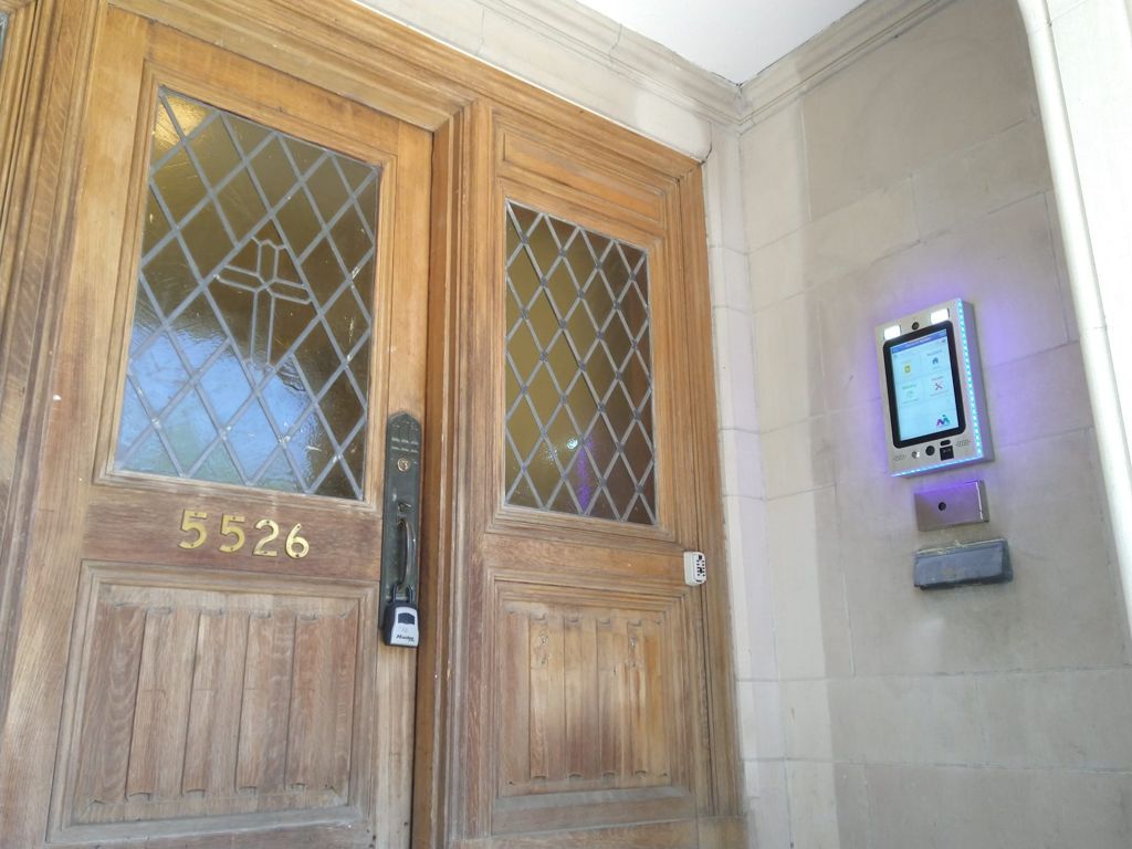 mvi keycom mounted on white stone wall by building entrance with brown wooden doors